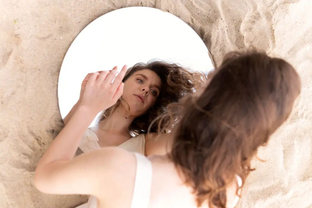 Woman admiring herself in the mirror with a gentle, loving gaze.