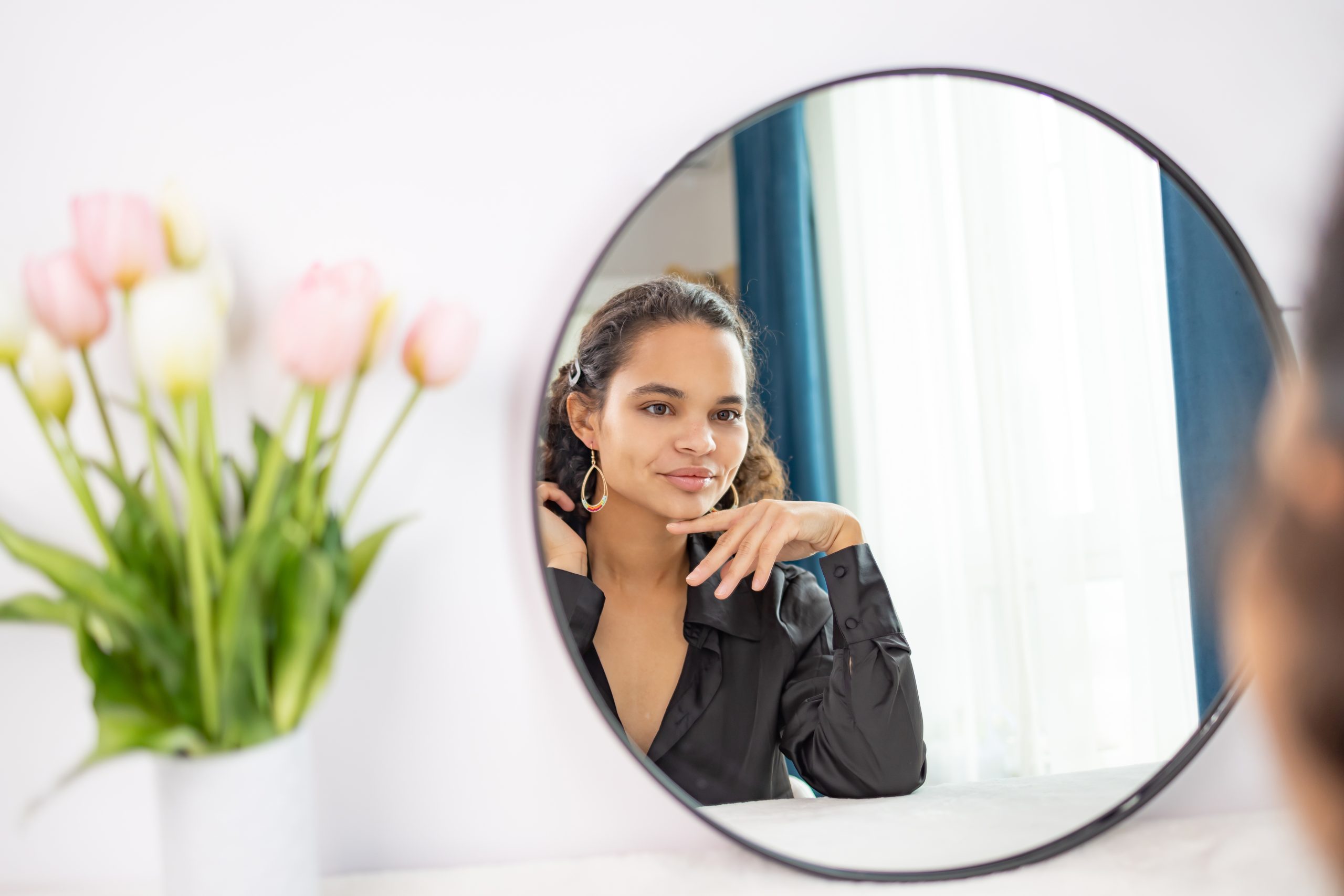 Woman looking at herself in the mirror with a gentle, accepting smile