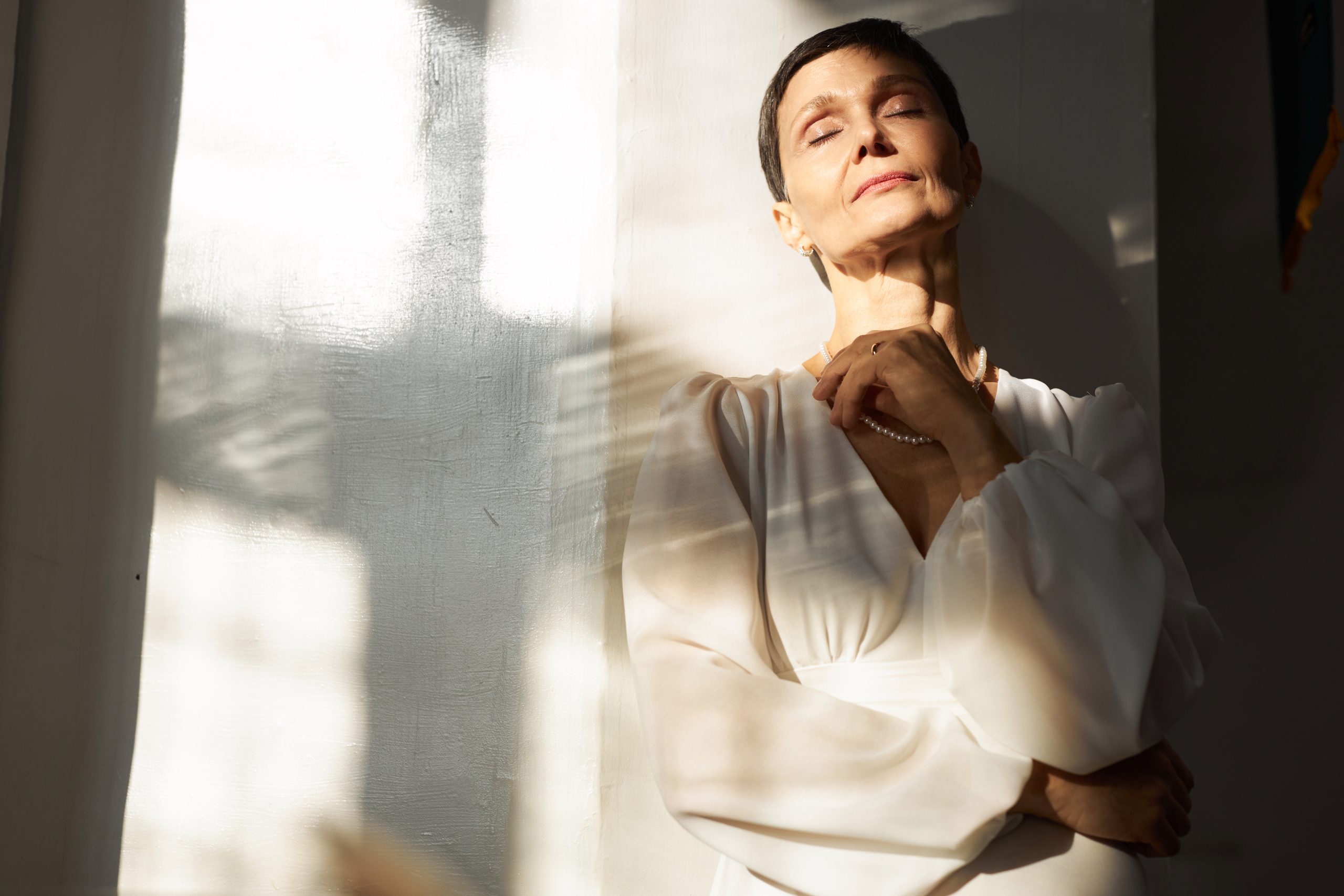Woman standing tall in nature, eyes closed, arms wide open