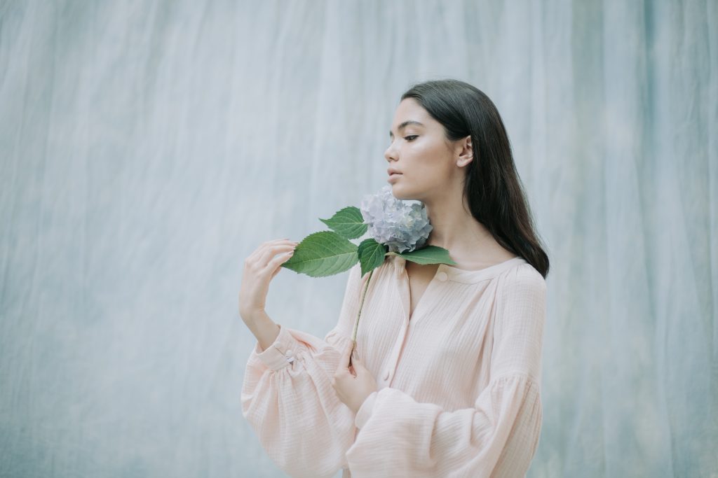 young-woman-holding-flower-standing-against-wall