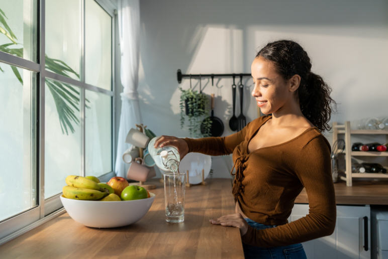 Woman in a home kitchen choosing between different foods and beverages, representing the link between diet and overall skin and body health