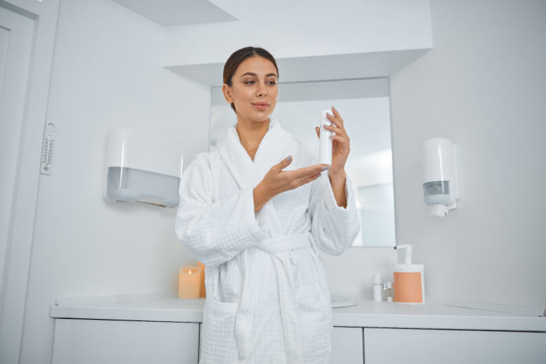 Woman standing in a clean bathroom surrounded by multiple personal hygiene products, symbolizing excessive intimate cleansing and its impact on vaginal health