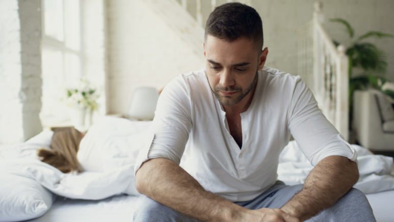 رجل يجلس بمفرده بوضعية تفكير أو توتر، يعبّر عن الضغط النفسي وتأثيره على العلاقة الحميمة.