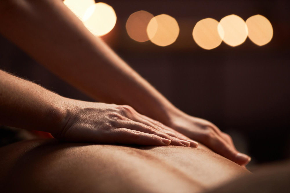Close-up of two hands gently resting on a partner’s back, symbolizing sensual massage as a form of presence, attention, and shared intimacy.